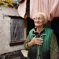 Nadiia, en äldre kvinna i Ukraina, står framför sitt enkla hem.