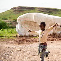 En pojke står på ett ben i ett flyktingläger.