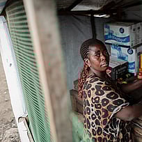 En kvinna står i sitt kök. Hon tittar allvarsamt mot kameran.