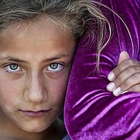 En flicka tittar in i kameran och kramar en annan persons arm.