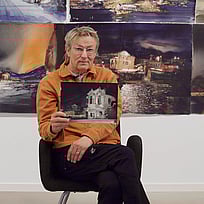 Lars Lerin sitter på en pall och visar upp en tavla.