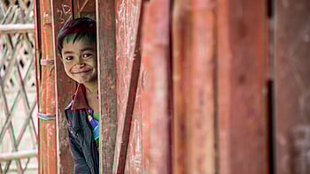 En pojke tittar ut bakom ett skynke.