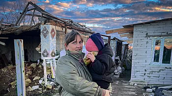 En kvinna står med sitt barn utanför sitt förstörda hem i Ukraina.