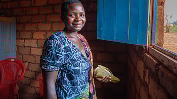 En kvinna ler mot kameran. Hon står i ett tegelhus och håller några sedlar i handen.