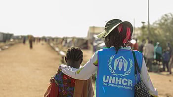 En kvinna med UNHCR-väst håller en arm runt en flicka.