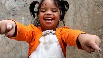 En flicka i orangea tröja och gul skrattar in i kameran.