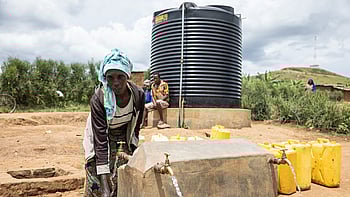 En kvinna hämtar vatten vid en vattencistern i ett flyktingläger i Uganda.