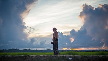 Kvinna som står på ett fält med en blå och solig himmel