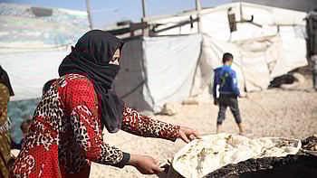 En kvinna i ett flyktingläger lagar bröd över en eld.