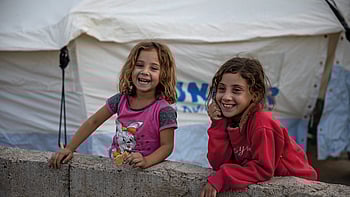 Två flickor ler mot kameran framför ett tält i Irak.