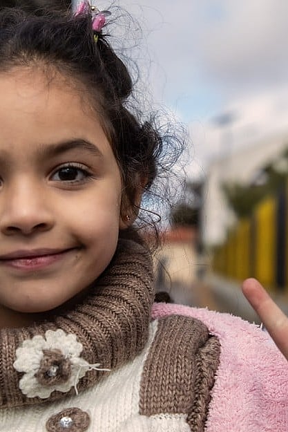 En flicka tittar in i kameran och gör fredstecken.