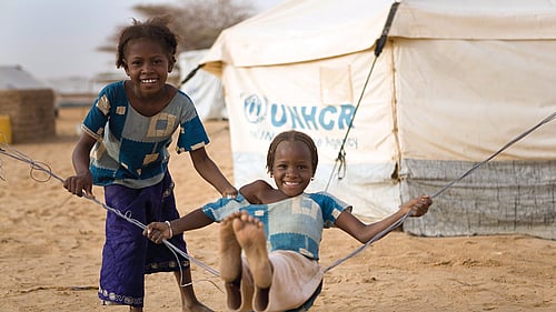 Två flickor som gungar utanför UNHCR-tält.