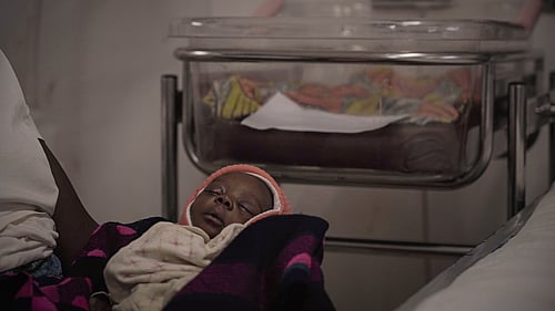 En bebis på ett sjukhus i flyktinglägret Nduta i Tanzania sover i sin mammas famn. På sjukhuset finns kuvöser för för tidigt födda barn, laboratorie, kylar för vaccin, blod och mediciner och engagerad vårdpersonal.