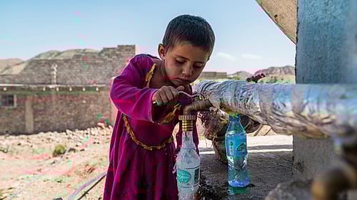 En pojke fyller på vatten från en kran i ett flyktingläger i Afghanistan.