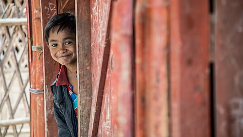 En pojke tittar ut genom ett skynke.