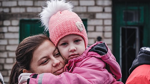 En mamma och dotter kramas och tittar in i kameran.