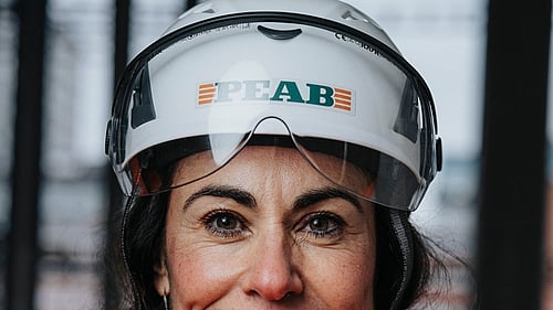 En kvinna klädd i byggkläder tittar in i kameran.