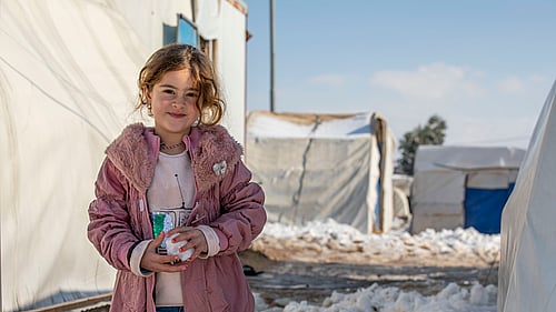 En flicka har kramat en snöboll. Hon tittar mot kameran.