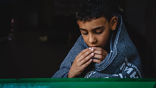 En syrisk pojke sitter insvept i en varm filt.