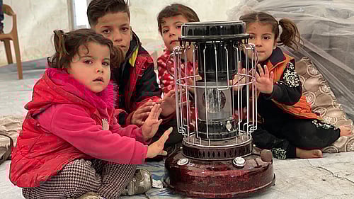 Barn på flykt från Syrien värmer händerna över en kamin i ett tältläger i Irak. Vill du värma en familj i vinter?