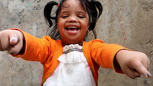 En glad flickar i orangea tröja tittar in i kameran.