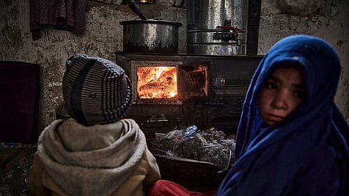 Två barn i Afghanistan värmer sig framför ett värmeelement.