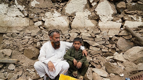 En pappa och son sitter bland stenar efter en jordbävning i Afghanistan 2025.