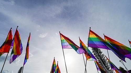 Flaggor som vajar i vinden, en av dem är en regnbågsflagga.