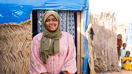 En kvinna sitter framför sitt hus. Hon ler mot kameran.