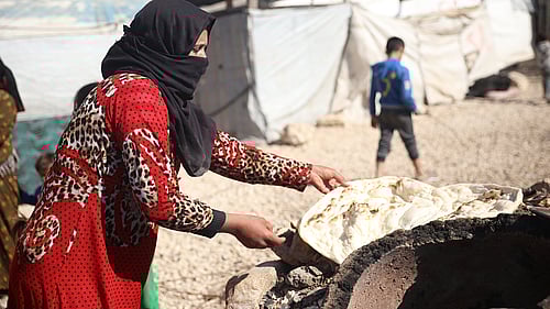 En kvinna i ett flyktingläger lagar bröd över en eld.