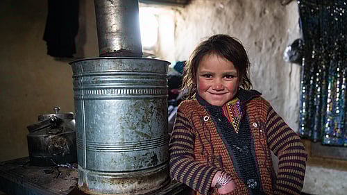 En 12-årig flicka står intill en värmekamin och ler mot kameran.