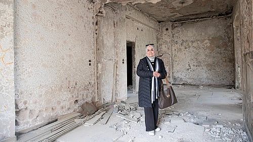 En kvinna står i sitt sönderbombade hus.