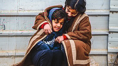 En mamma och pojke på flykt kramas under en filt.