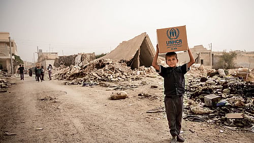 En pojke bär ett nödpaket på huvudet på en tom gata i Syrien. Köp gåvobevis Nödpaket och rädda liv.