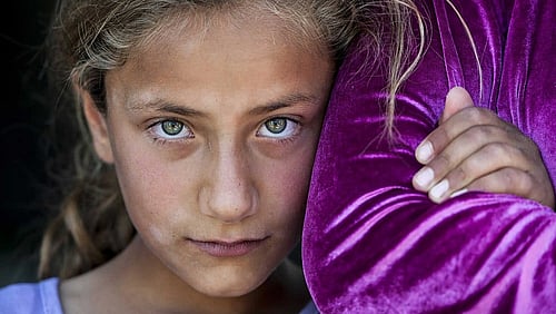 En flicka tittar in i kameran och kramar en annan persons arm.