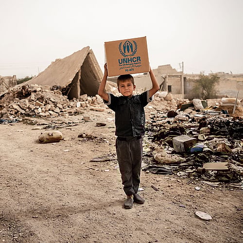 En pojke bär ett nödpaket på huvudet på en tom gata i Syrien. Köp gåvobevis Nödpaket och rädda liv.