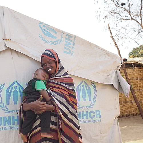 En kvinna och hennes barn framför ett UNHCR-tält.
