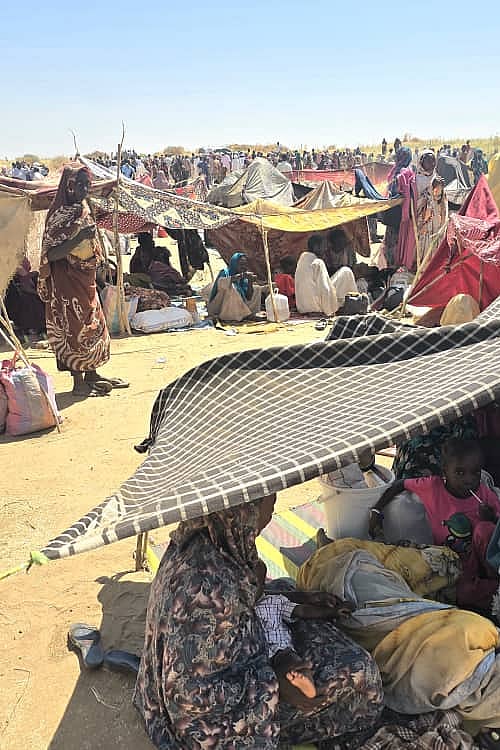 Människor som flytt kriget i Sudan sitter utspridda på marken.