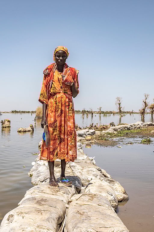 En kvinna står mellan två översvämmade fält i Sydsudan.