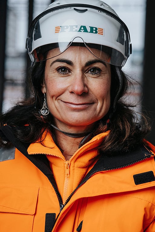 En kvinna klädd i byggkläder med hjälm. Hon tittar in i kameran.