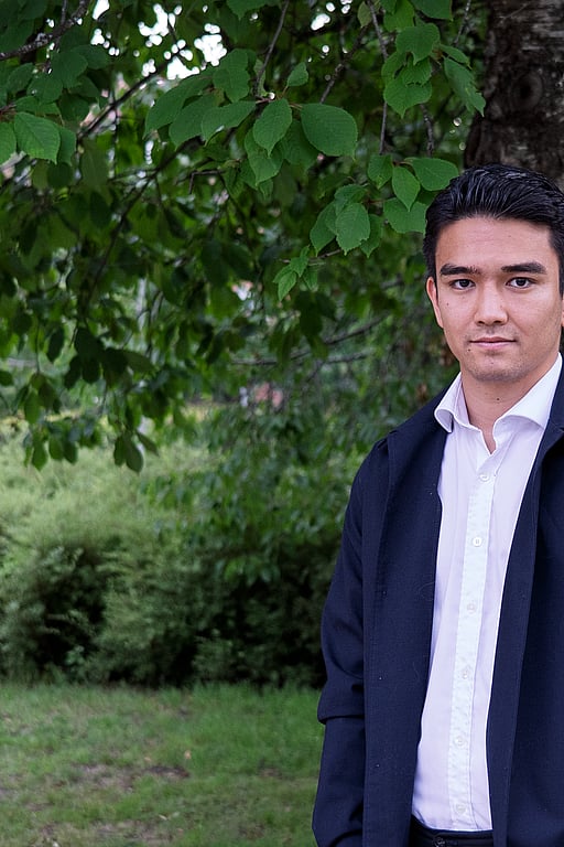 En ung man står framför en stor grönskande buske.