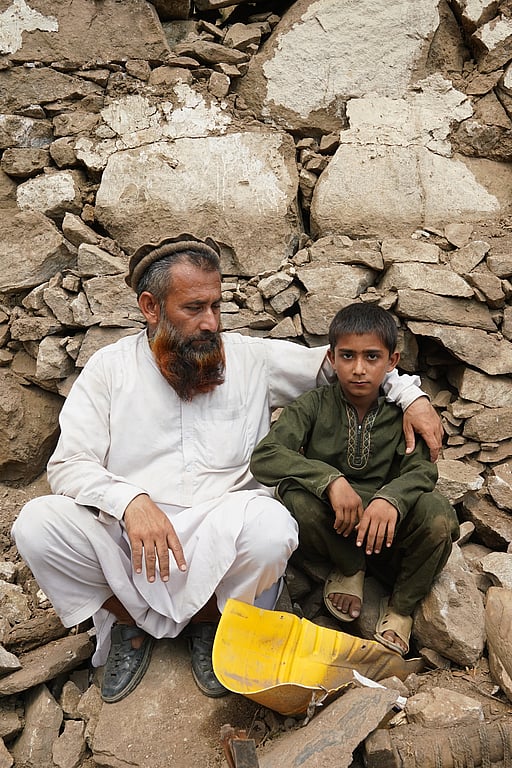 En pappa och son sitter bland stenar efter en jordbävning i Afghanistan 2025.