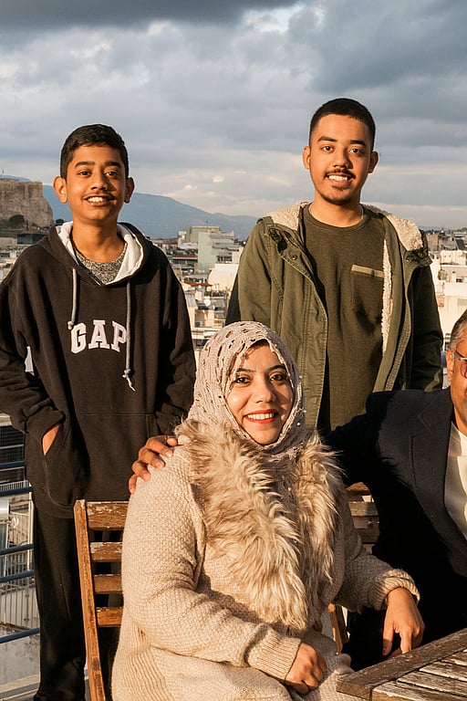 En familj med fyra personer tittar in i kameran och ler. I bakgrunden syns greklands huvudstad Aten.