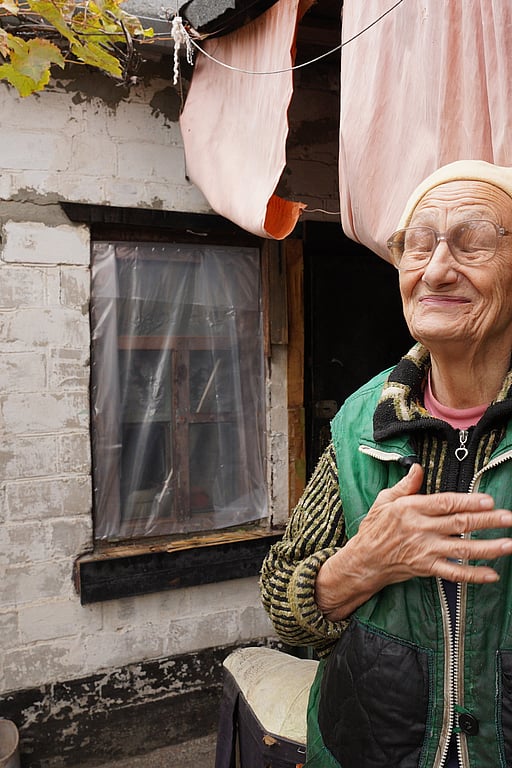 Nadiia, en äldre kvinna i Ukraina, står framför sitt enkla hem.