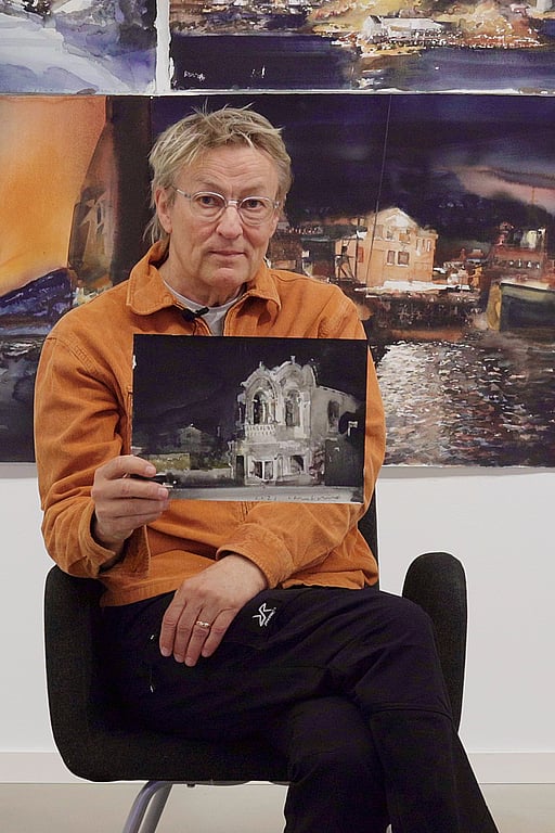 Lars Lerin sitter på en pall och visar upp en tavla.