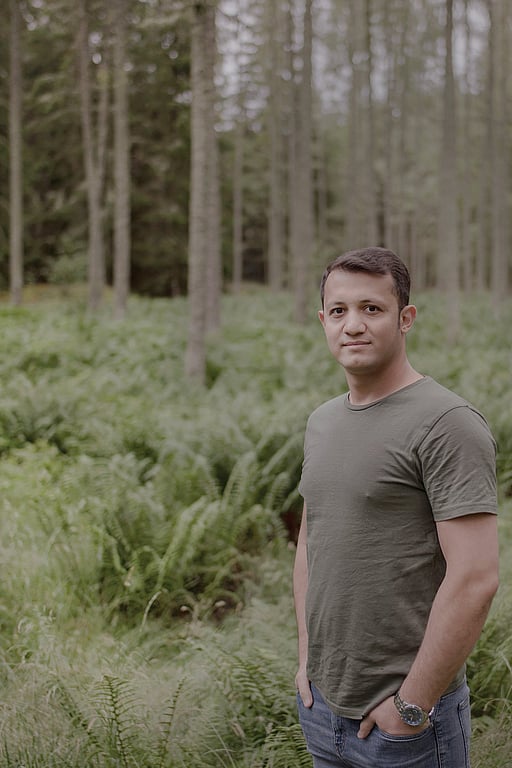 En man i grön tröja står i en skog.