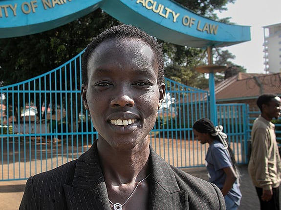 En kvinna står framför ingången till ett universitet. Hon ler mot kameran.