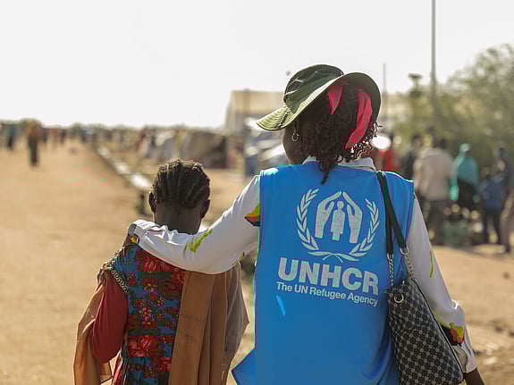 En kvinnlig UNHCR-medarbetare lägger armen runt axlarna på ett barn.