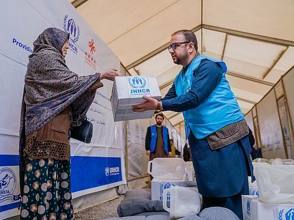 En UNHCR-medarbetare lämnar över en kartong med förnödenheter i Afghanistan.