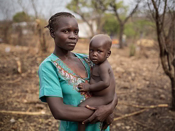 En kvinna håller sitt lilla barn i famnen och tittar in i kameran.